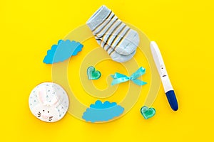 Pregnancy and preparation for childbirth. Babyshower. Pregnancy test near socks and hearts yellow background top view