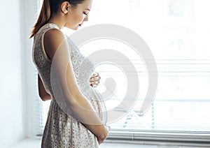 Pregnancy, rest, people and expectation concept - close up of happy smiling pregnant woman touching her belly at home