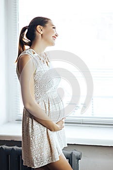 Pregnancy, rest, people and expectation concept - close up of happy smiling pregnant woman touching her belly at home