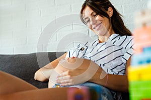 Pregnancy, rest, people and expectation concept. Happy pregnant woman touching her belly at home