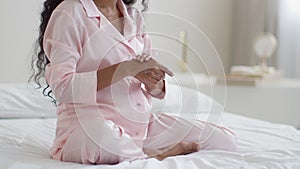 Pregnancy and skin care. Unrecognizable pregnant woman rubbing moisturizing cream on hands, sitting on bed, empty space