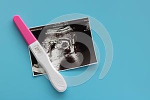 Pregnancy test and baby ultrasound photo scan photo on blue background.