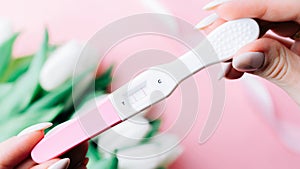 Pregnancy test couple. Positive woman pregnant test in hands with pink silk ribbon on tulips flower pink background. New