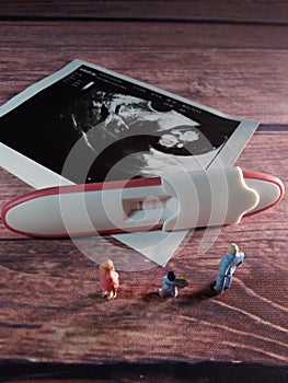 Pregnancy test pack positive result at wooden table and family miniature figure