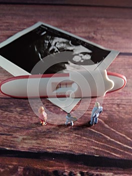 Pregnancy test pack positive result at wooden table and family miniature figure