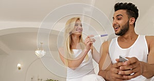 Pregnancy test positive result, couple sitting bed mix race man woman happy smile embrace morning bedroom