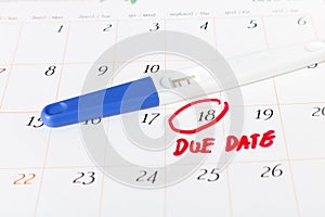 Pregnancy test with positive result lying on calendar background