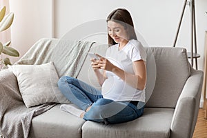Pregnancy Tracker App. Smiling Young Pregnant Lady Using Smartphone At Home