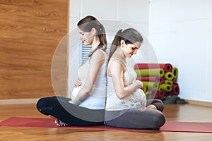 Pregnancy Yoga, Fitness concept. Portrait of two young models. They sit on the floor holding their hands with their stomachs