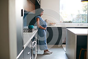Pregnant African American Woman Standing In Kitchen At Home With Hot Drink
