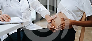 Pregnant african woman has appointment with doctor at clinic. Male gynaecologist OB GYN medic specialist with stethoscope listens photo