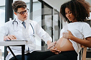 Pregnant african woman has appointment with doctor at clinic. Male gynaecologist OB GYN medic specialist with stethoscope listens