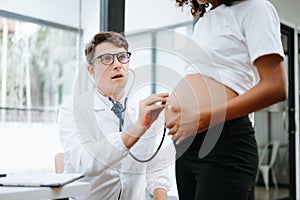 Pregnant african woman has appointment with doctor at clinic. Male gynaecologist OB GYN medic specialist with stethoscope listens