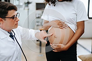 Pregnant african woman has appointment with doctor at clinic. Male gynaecologist OB GYN medic specialist with stethoscope listens