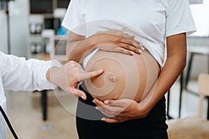 Pregnant african woman has appointment with doctor at clinic. Male gynaecologist OB GYN medic specialist with stethoscope listens photo