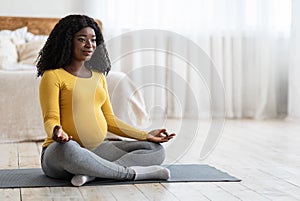 Pregnant african woman meditating in lotus position at home