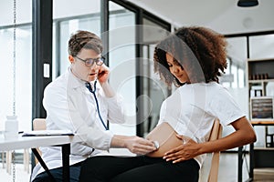 Pregnant african woman has appointment with doctor at clinic. Male gynaecologist OB GYN medic specialist with stethoscope listens photo