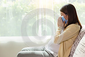 Pregnant Asia mother get sick of cold or flu and coughing Young pregnant asian woman in face mask stay alone at home for self