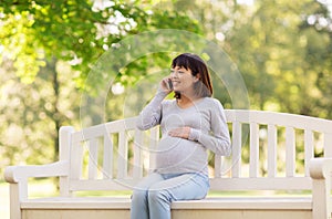 Pregnant asian woman calling on smartphone at park