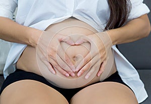 Pregnant asian woman holding gesture heart symbol shape belly.