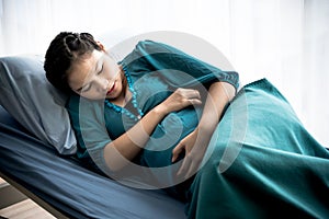 Pregnant Asian woman is lying on a patient`s bed,