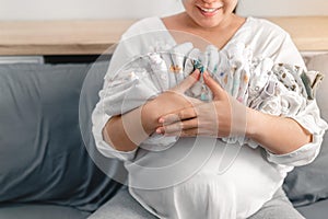 Pregnant asian woman smiling and  huging baby clothes for planning new born baby, Prepare before Give birth baby concept