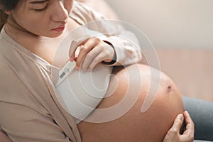 Pregnant asian woman used digital thermometer on bed at morning, Sick female with high fever, Selective focus, Healthy and