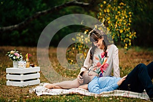 Pregnant beautiful woman with her handsome husband sweetly resting outdoors in the autumn on picnic.