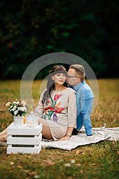 Pregnant beautiful woman with her handsome husband sweetly resting outdoors in the autumn on picnic.