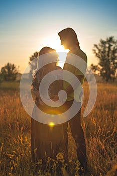 A pregnant beautiful woman with her husband on nature landscape smiling and touching her belly with love and care. Happy