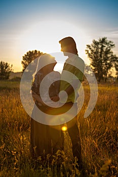 A pregnant beautiful woman with her husband on nature landscape smiling and touching her belly with love and care. Happy