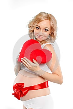 Pregnant beautiful woman holding red heart pillow in her hands isolated on white background