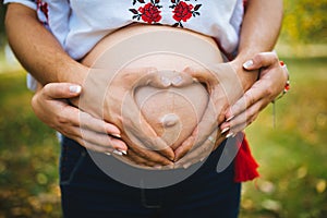 Pregnant Belly with fingers Heart symbol. Beautiful Young Pregnant Woman and Her Husband Together Caressing Her Pregnant Belly.