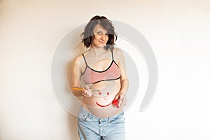 Pregnant belly girl with a smile on your stomach. The pregnant woman is having fun with paints in her hands. The joy and