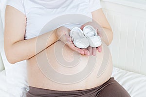 Pregnant belly with a pair of white shoes