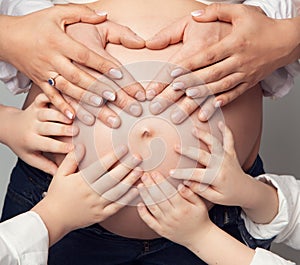 Pregnant Belly with Parents and Kids Hands. Father Heart shaped Hands and little Children touching Mother Pregnancy Abdomen