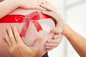 Pregnant belly with red ribbon and hands of mom and dad