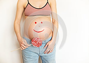 Pregnant belly with a smile on your belly. Pregnant woman with a large lolli pop in her hands is having fun. The joy and happiness