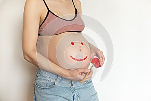 Pregnant belly with a smile on your stomach. The pregnant woman is having fun with paints in her hands. The joy and
