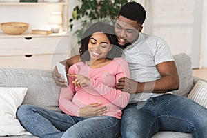 Pregnant black couple using smartphone together at home