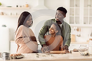 Pregnant Black Woman And Her Husband And Daughter Baking Indoors