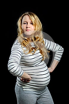 Pregnant blond girl with curly hair looks angrily on black background