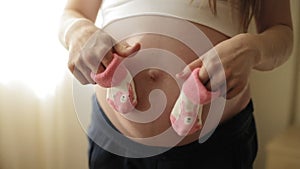 Pregnant blonde woman playing with pink baby booties on belly. Close up.