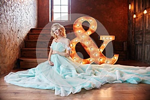 Pregnant bride blonde is preparing to become a mother and wife. Long turquoise dress on a girl body. Curly hair and a beautiful