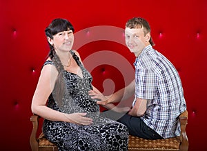 Pregnant brunette woman with husband on red background. Couple