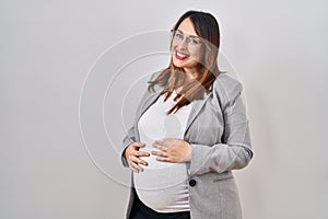 Pregnant business woman standing over white background with serious expression on face