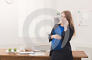 Pregnant business woman talking on phone at office