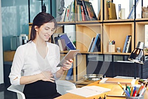 Pregnant business woman working at office motherhood sitting holding digital tablet