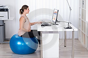 Pregnant Businesswoman On Fitness Ball Looking At Graph