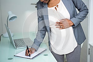 Pregnant businesswoman writing on notebook